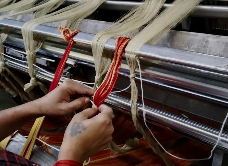 Mani di un artigiano indiano che lavorano fili di cashmere e seta su un telaio per la produzione di un cappotto Anirav Brand