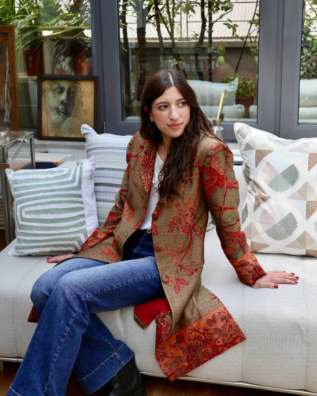 modella indossa un cappotto di anirav brand seduta sul divano. cappotto delhi verde olive in cashmere e seta di bambù.