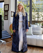 Cappotto lungo cashmere seta Delhi blu indossato in un ambiente moderno con piante e arredi eleganti.