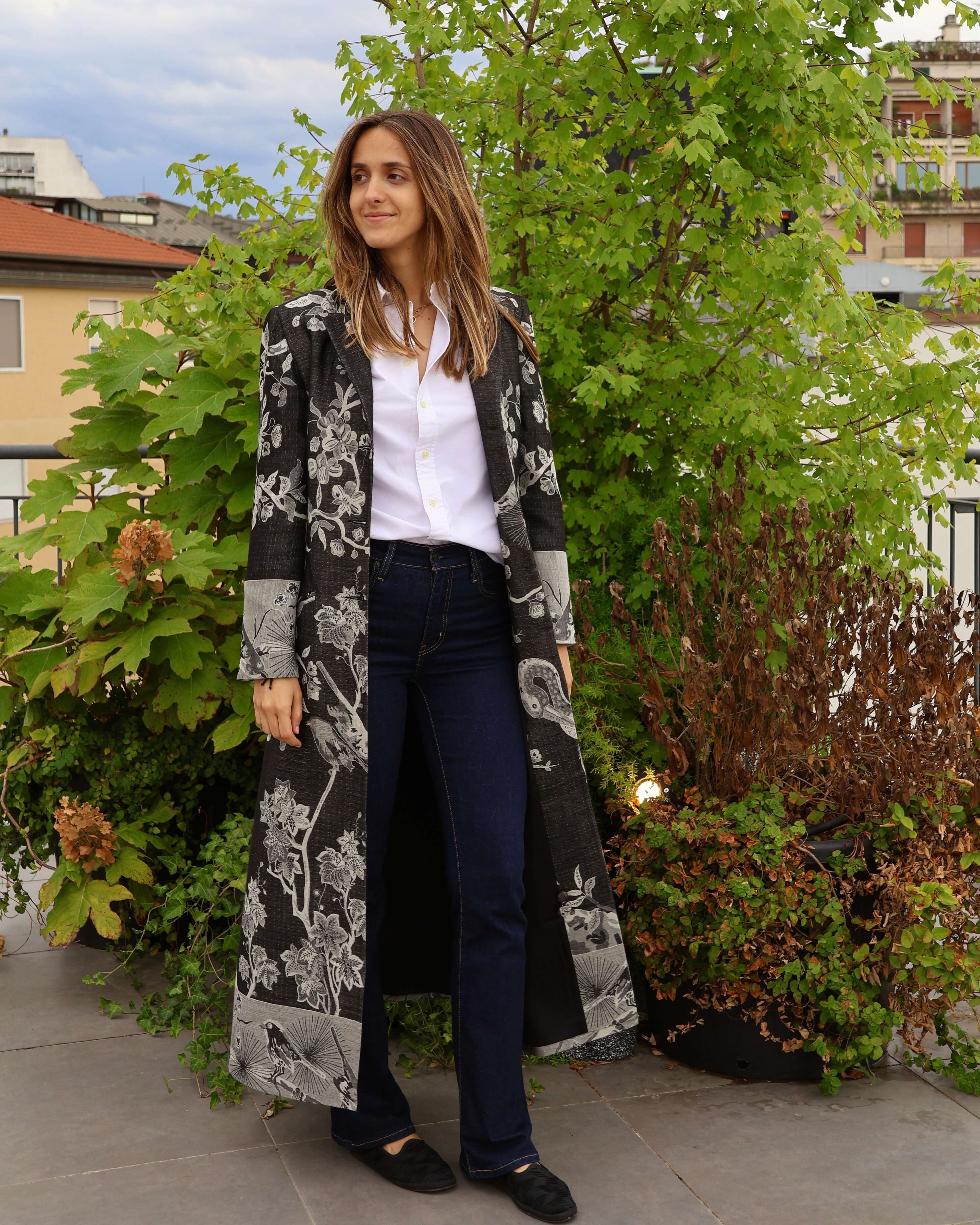 Cappotto Delhi Nero lungo in cashmere e seta di bambù, moda artigianale indossato da una donna in un ambiente naturale.
