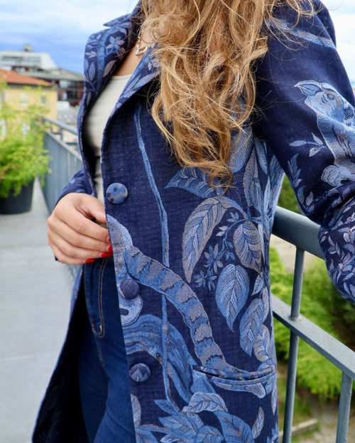Cappotto lungo cashmere seta Delhi Blu, dettagli floreali e naturali, indossato con stile su una terrazza.