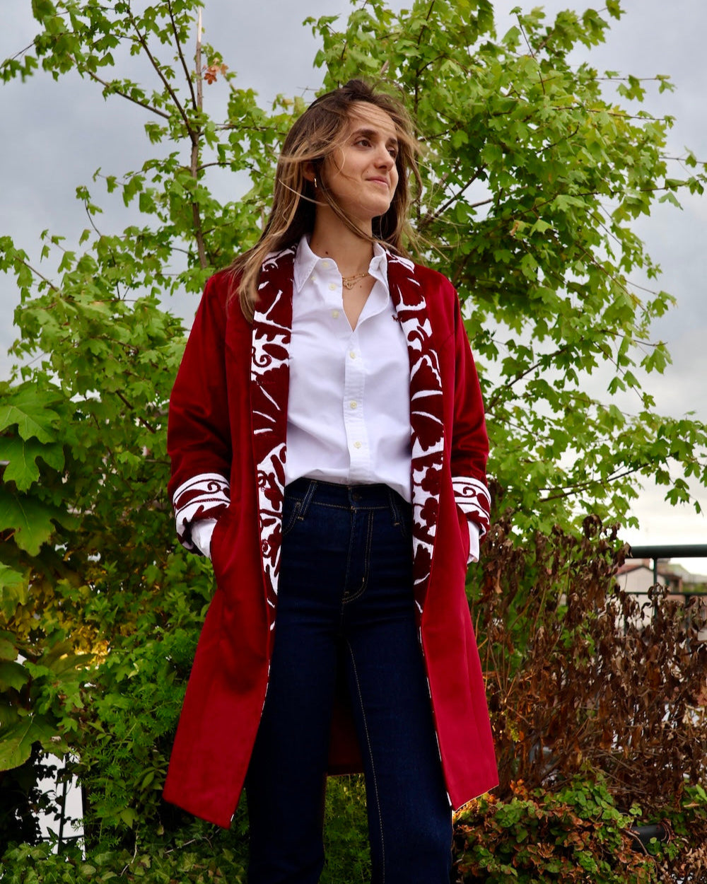Modella con indosso il cappotto Jaipur di Anirav Brand, in piedi davanti a una pianta verde in un giardino.