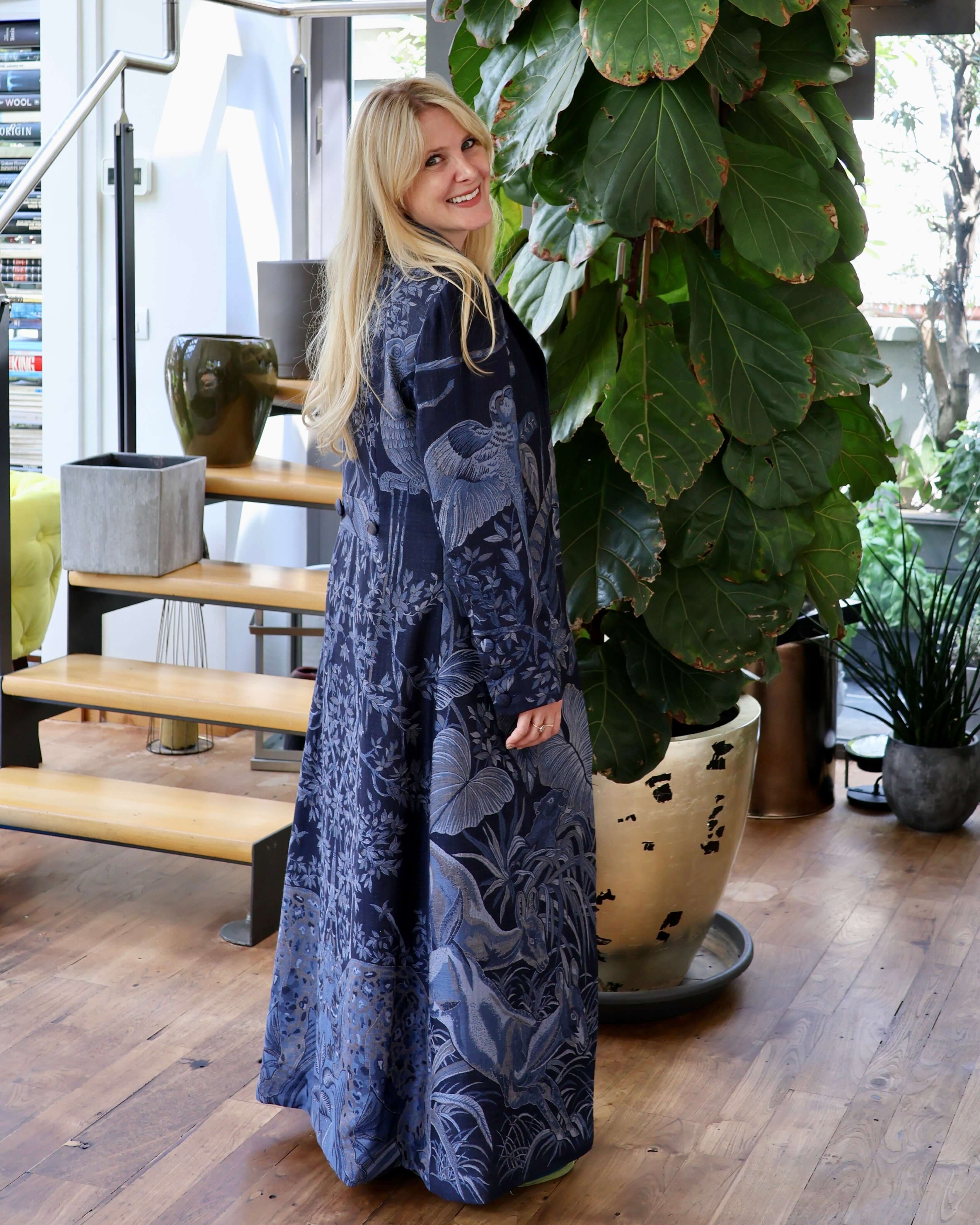 Cappotto lungo cashmere seta Delhi Blu indossato da una donna in un ambiente elegante con piante.